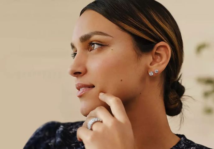 Model with brown hair wearing black blouse, lab-grown low dome seven stone ring, low dome eternity ring and two pairs of diamond stud earrings